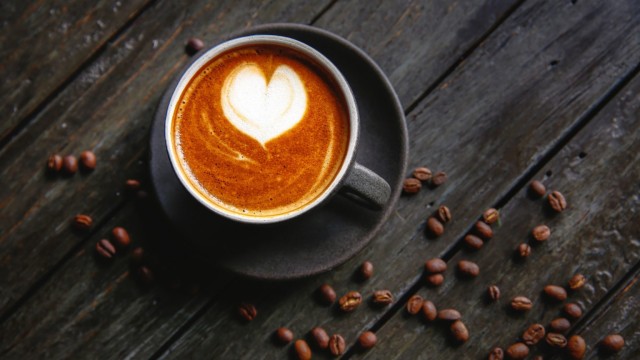 Een afbeelding van een kop koffie met in de schuimlaag een hartje en om het kopje heen liggen koffiebonen