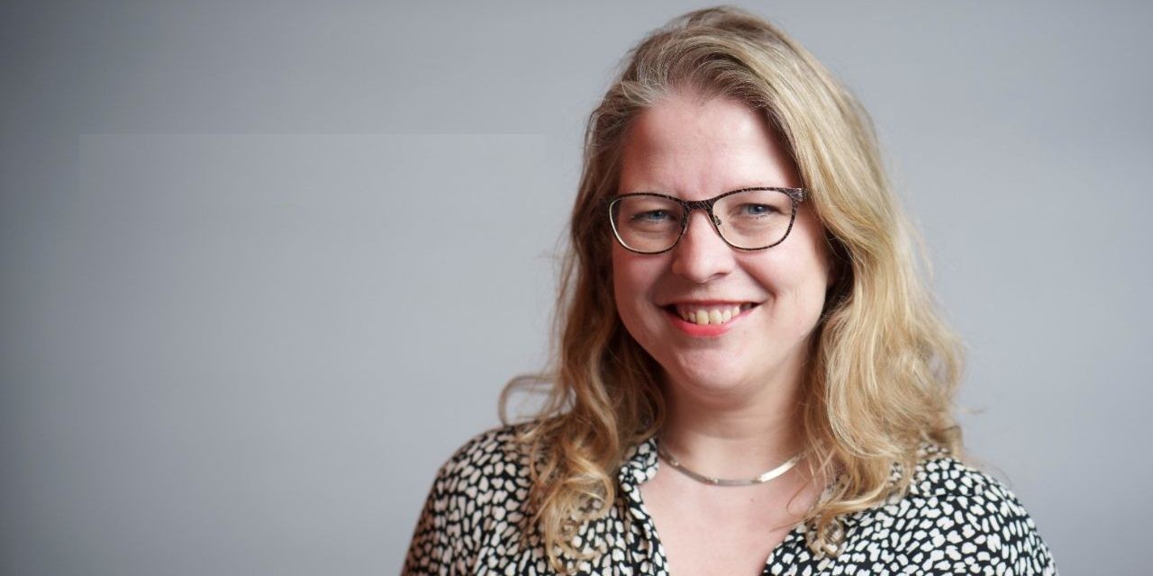Portret van een vrouw met blond haar een bril die glimlacht naar de camera