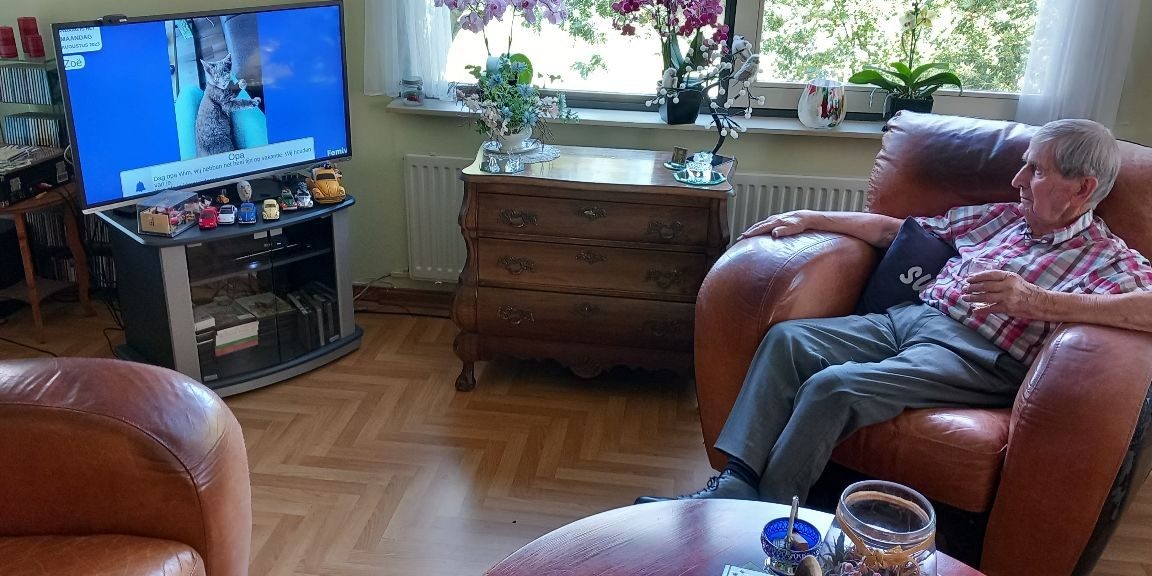 Man in fauteuil kijkt naar televisiescherm met een foto van een kat
