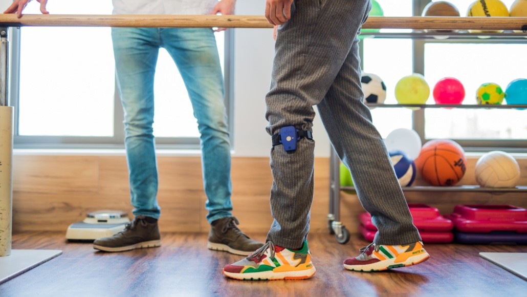 Persoon loopt met een Cue2walk-apparaat in een revalidatie-omgeving.