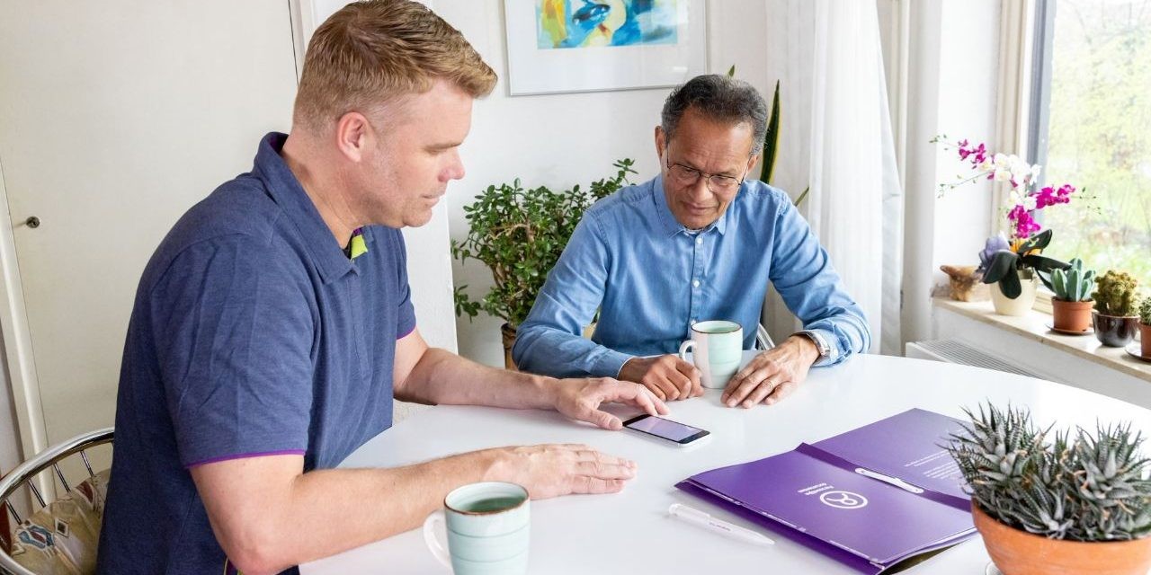 Twee mannen aan een ronde tafel kijkend naar een mobiele telefoon