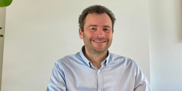 Man met kort bruin haar en een blauwe blouse op een witte achtergrond.