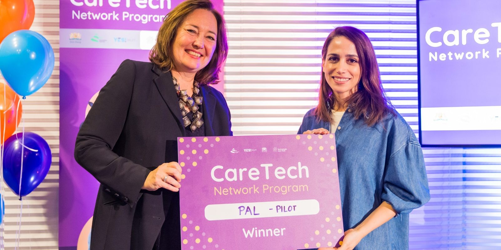 Twee vrouwen houden glimlachend een bord vast met de tekst ‘Pal - winnaar’