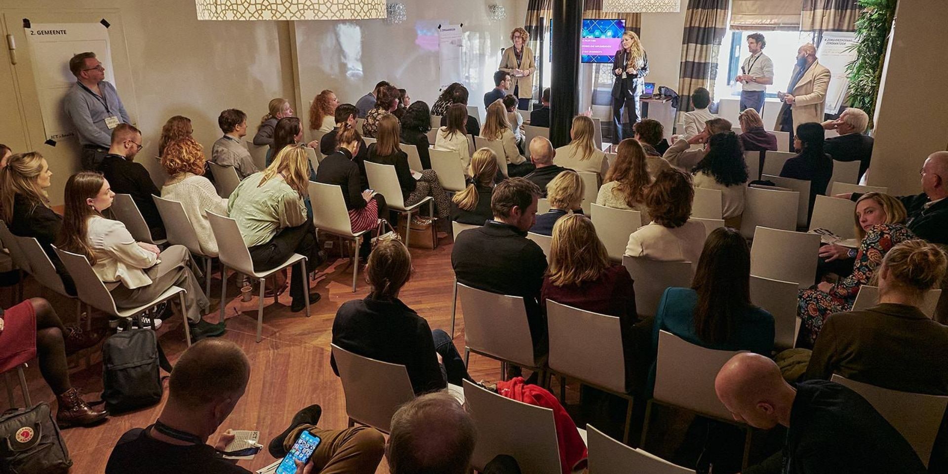 Deelnemers zitten in een ruimte in theater-opstelling