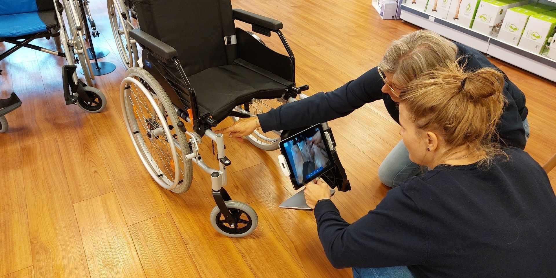Twee mensen in een winkel richten een tablet naar een rolstoel om iets aan te duiden